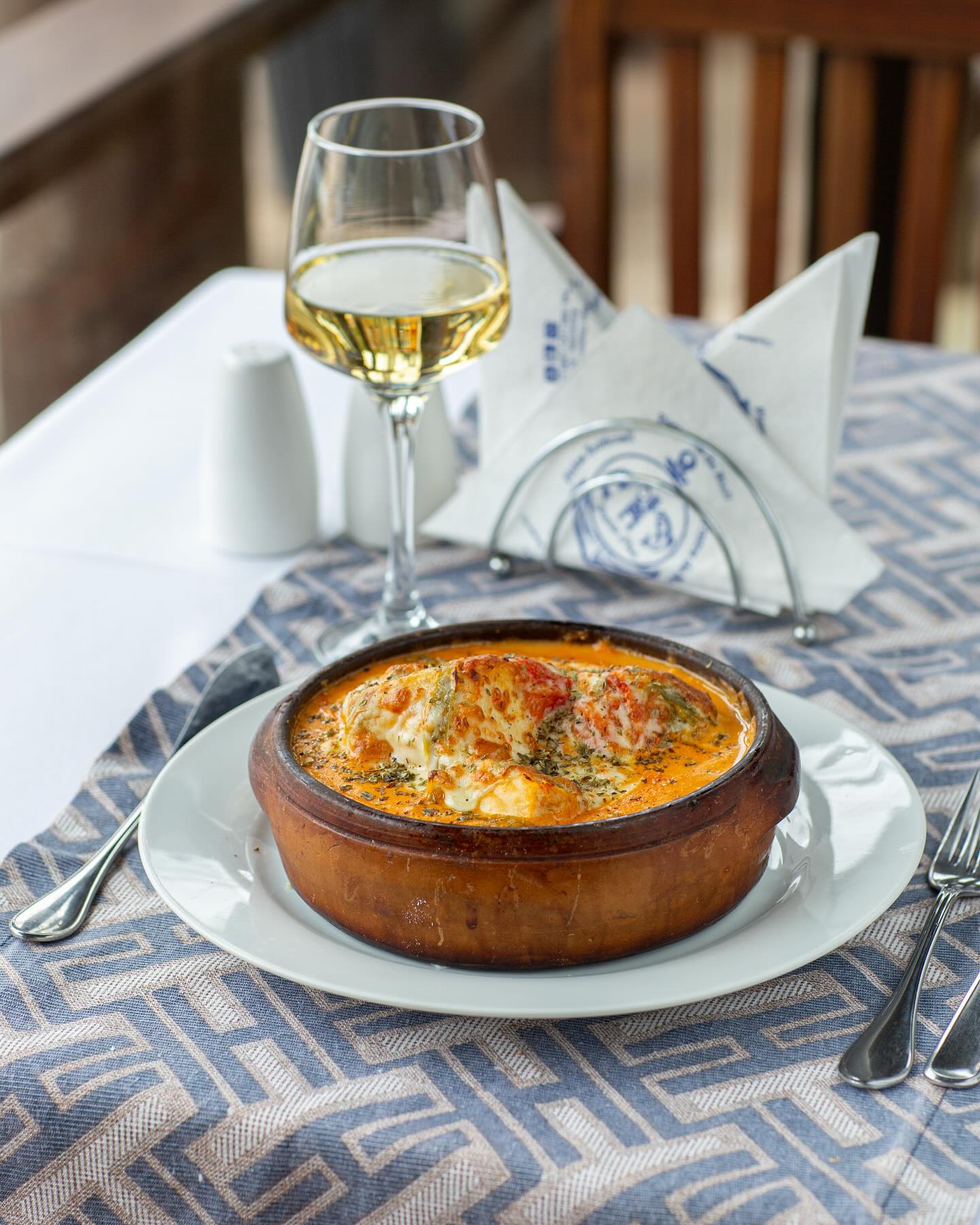Cazuela gratinada en cazuela de barro, servida en la mesa con vino blanco
